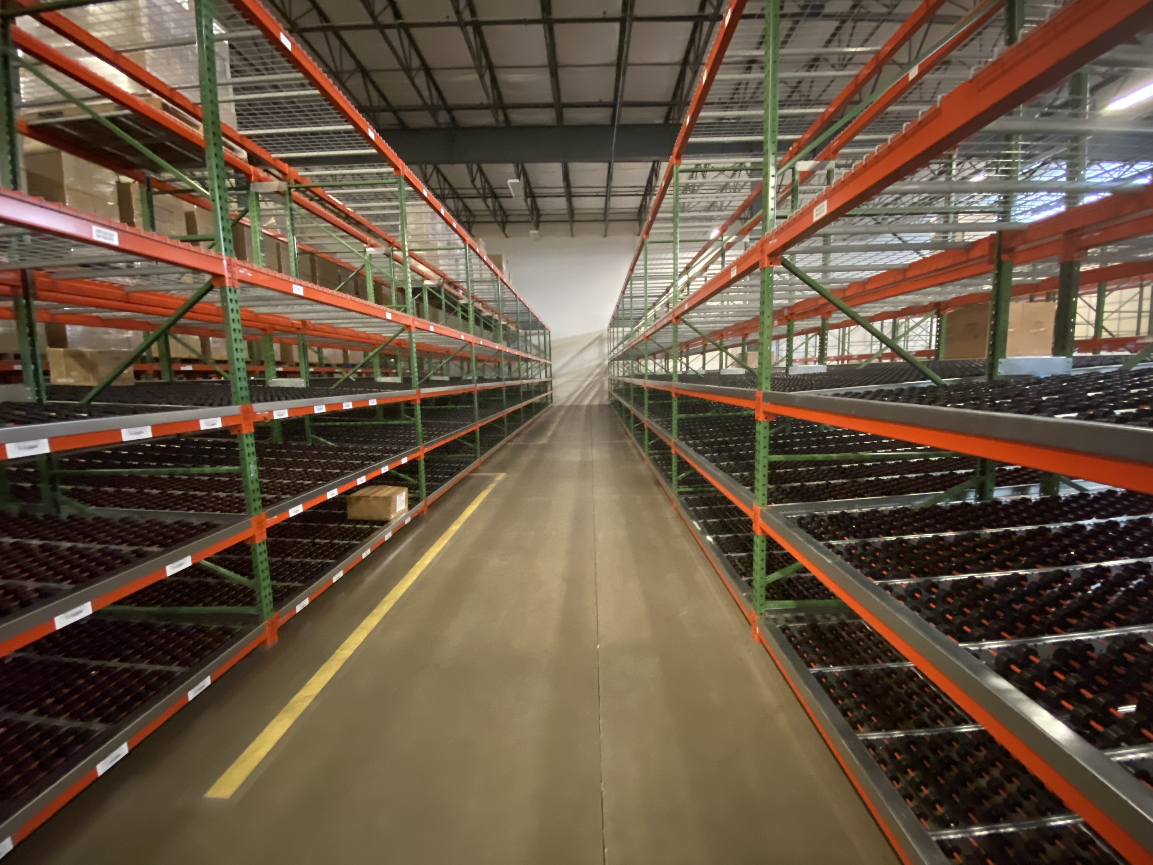Looking down an aisle on a warehouse with green and orange carton flow racking on both side