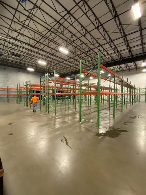 Green and orange pallet racking ebing stalled by one man in a warehouse.